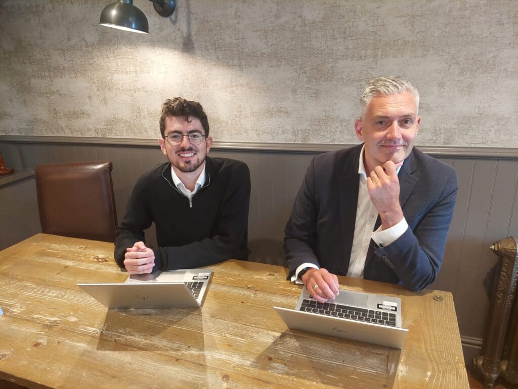 David Smith MP and Theo from his team smile at the camera. They are in the Craster Arms in Beadnell with laptops and notepads on the table in front of them