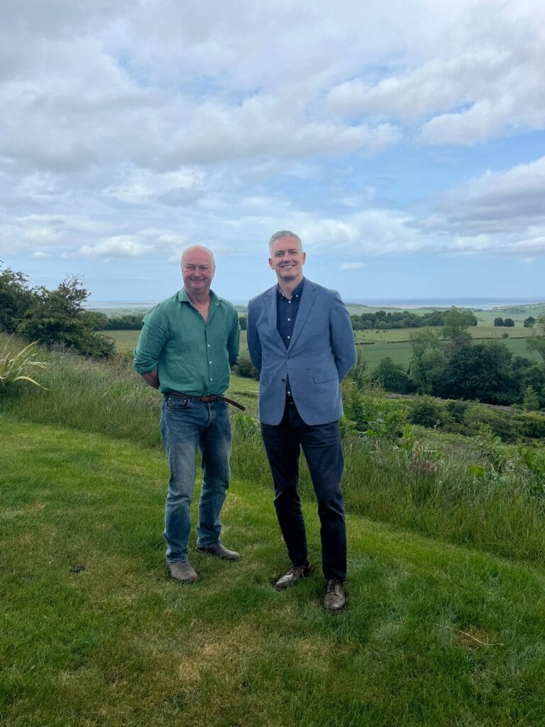 David Smith stands with John, a local farmer, in a grassy field in Northumberland.